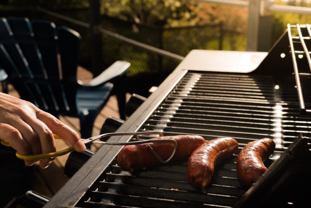 Person holding sausage on barbecue grill