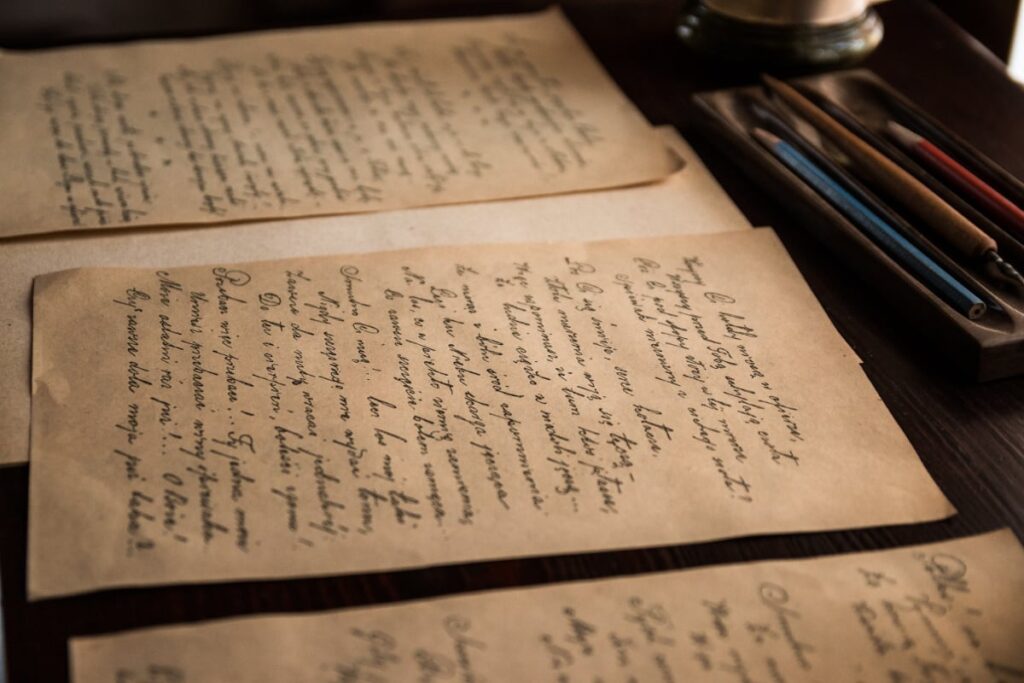 Photo of old hand written letters on a desk with some pencils and pens